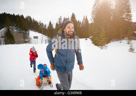 Giovane uomo tirando figli sul toboga in paesaggi innevati, Elmau, Baviera, Germania Foto Stock