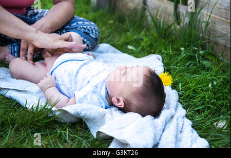 Ritagliato colpo di donna di applicare la crema durante la modifica di baby figlio il pannolino in giardino Foto Stock