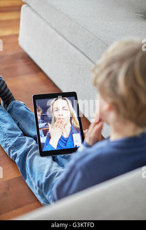 Ragazzo seduto sul pavimento soffia un bacio alla madre sulla tavoletta digitale video chiamata Foto Stock