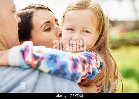 Sulla spalla vista della madre baciare sorridente figlia sulla guancia Foto Stock