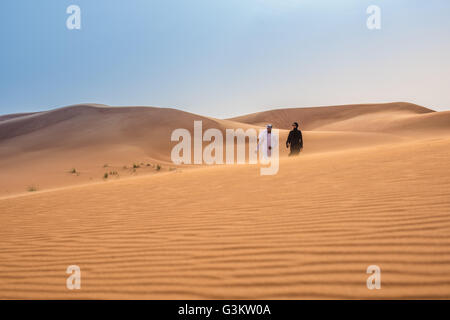 Vista in lontananza giovane indossando il tradizionale del medio oriente a piedi vestiti sulle dune del deserto, Dubai, Emirati Arabi Uniti Foto Stock