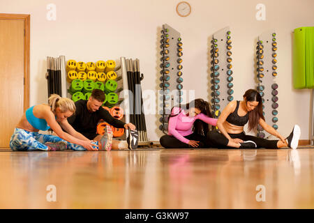 Persone in palestra seduta sul pavimento della gamba facendo esercizi di stretching Foto Stock