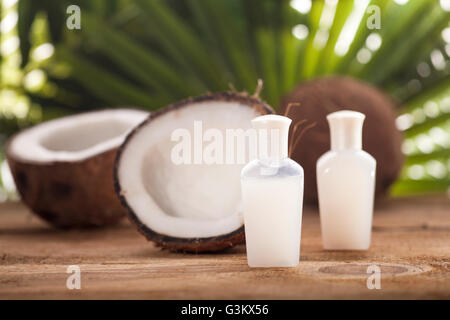 Noci di cocco e olio di noce di cocco sul tavolo di legno, su sfondo natura Foto Stock