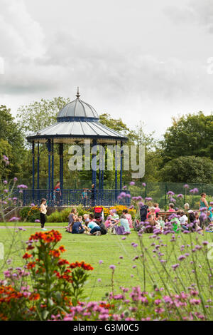 La gente nel parco di fronte al palco per spettacoli presso la War Memorial Park a Romsey, Hampshire, Inghilterra, Regno Unito, Europa Foto Stock