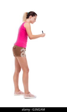 Vista posteriore della scrittura bella donna. Vista posteriore di raccolta persone. vista posteriore di persona. Isolato su sfondo bianco. Ragazza bionda in pantaloncini corti e camicetta rosa sorge e disegna un pennarello. Foto Stock