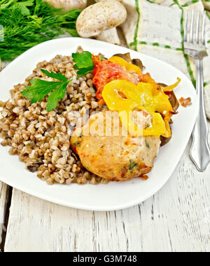 Cotoletta di carne di tacchino con il grano saraceno, funghi, pomodori e peperoni nel piatto, prezzemolo, un asciugamano e una forcella sullo sfondo Foto Stock