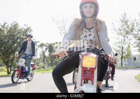Gruppo di amici i ciclomotori a cavallo lungo la strada, giovane pilota femmina in primo piano Foto Stock