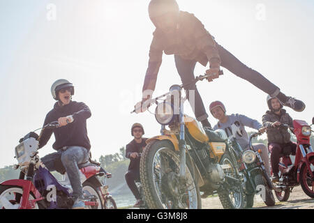 Gruppo di amici i ciclomotori a cavallo lungo la strada, l'uomo a metà in aria, facendo stunt Foto Stock