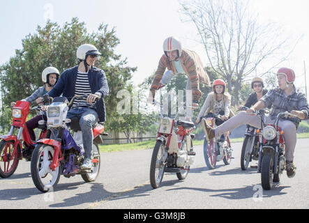 Gruppo di amici i ciclomotori a cavallo lungo la strada, l'uomo a metà in aria, facendo stunt Foto Stock