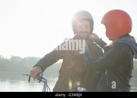 Giovane donna aiuta l uomo messo sul casco, sorridente Foto Stock