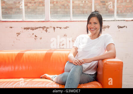 Donna seduta sul divano sorridente Foto Stock