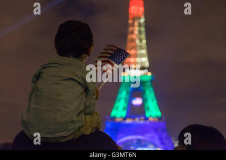 Parigi, Francia. 13, Giugno, 2016. Un giovane bambino seduto sulle spalle di suo padre onde una bandiera americana mentre si guarda la Torre Eiffel illuminata con i colori dell'arcobaleno per mostrare il loro sostegno alle vittime del tiro di Orlando. Credito: David Bertho / Alamy Live News Foto Stock