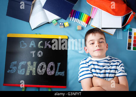 Bambino giacente sulla coperta blu con lavagna a fogli mobili e accessori per la scuola Foto Stock