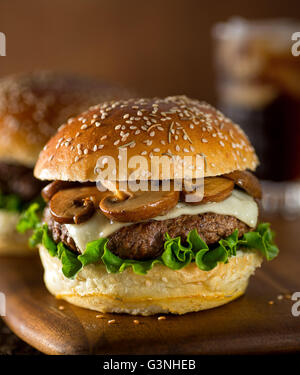 Un delizioso hamburger gourmet conditi con formaggio svizzero e Funghi Fritti su un rosmarino semi di sesamo bun. Foto Stock