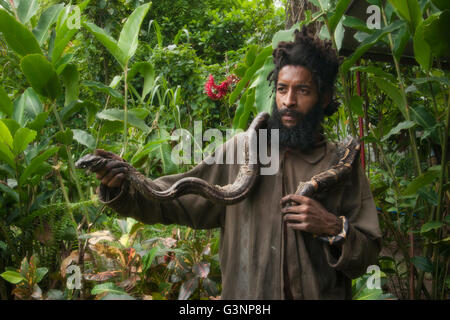 Uomo in dreadlocks tenendo la sua pet Boa Constrictor snake, Wotten Waven, Roseau Valley, sud della Dominica, West Indies francese Foto Stock