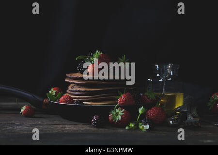 Frittelle di cioccolato nella pentola arrugginita con fragole, more e miele a sfondo scuro con luce mistica Foto Stock