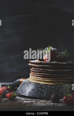 Frittelle di cioccolato nero in padella con frutta organica come fragole, more e zucchero semolato sul vecchio tavolo in legno Foto Stock