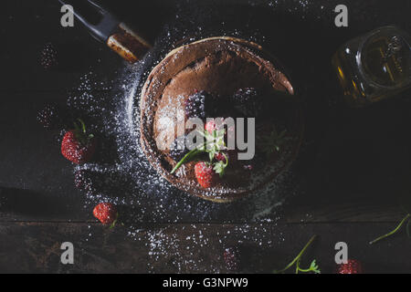 Frittelle di cioccolato in pentola arrugginita con frutta organica come fragole, more e zucchero semolato sul vecchio tavolo in legno, piatto l Foto Stock