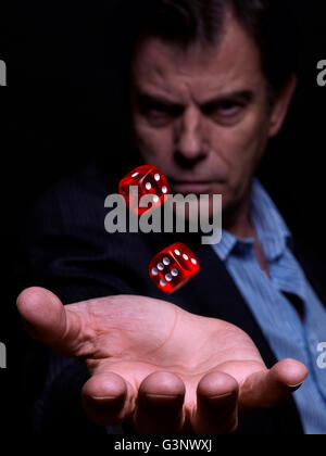L'uomo, in un abito senza cravatta, tenendo dadi rossi, prendendo un rischio su sfondo nero Foto Stock