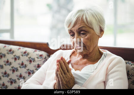 Senior donna orante nel soggiorno Foto Stock