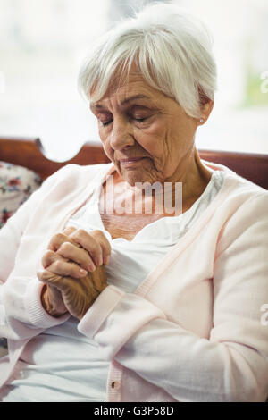 Senior donna orante nel soggiorno Foto Stock