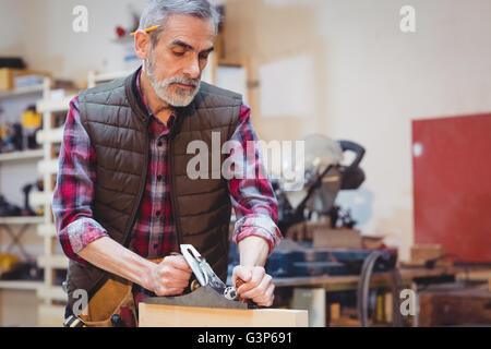 Ritratto di falegname perfezionando asse di legno formano con un attrezzo di lavoro Foto Stock