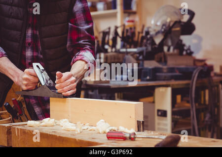Ritratto di falegname perfezionando asse di legno formano con un attrezzo di lavoro Foto Stock