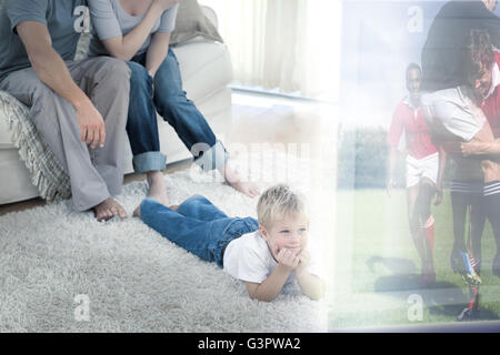 Immagine composita di carino ragazzo disteso sul tappeto è guardare lo sport in televisione nella parte anteriore dei suoi genitori Foto Stock