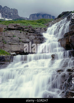 Stati Uniti d'America, Montana, il Parco Nazionale di Glacier, Cascata sul pagliaio Creek sotto storm-avvolta picchi di il muro del giardino. Foto Stock