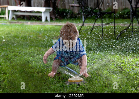 Baby Boy caucasica e Madre a giocare nel suo cortile interno con giardino irroratore Foto Stock