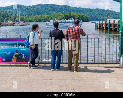 Tre oriente turisti asiatici guardare le imbarcazioni sul lago in una giornata di sole in riva al lago di Windermere Bowness Cumbria Foto Stock