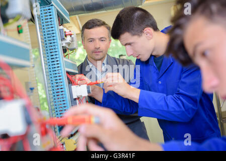 Insegnante osservando gli studenti al lavoro su circuiti elettrici Foto Stock