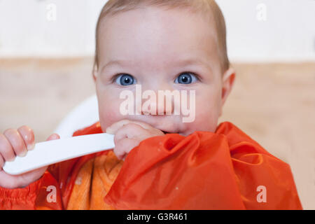 8 mese baby boy avente il suo cereale poltiglia. Indossa un cartellino arancione. Cercando di mangiare in modo indipendente Foto Stock