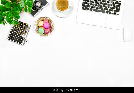 Creatrice femminile home office workplace. Caffè, amaretto cookies, computer portatile e pianta verde su bianco sfondo tabella Foto Stock