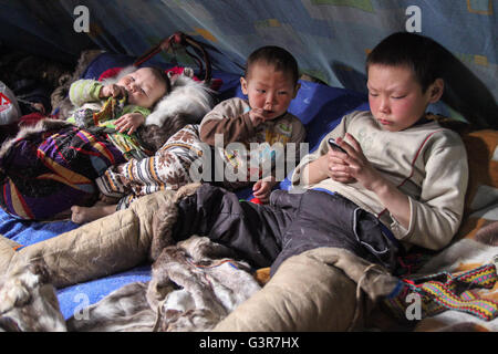 N. bambini giocato con un telefono cellulare all'interno della chum-abitazioni tradizionali dei Nenets gli allevatori di renne. Foto Stock