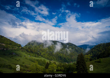 Paesaggio con vecchie case in legno e le montagne coperte da nubi. Le montagne e le nuvole nella foresta pluviale Foto Stock
