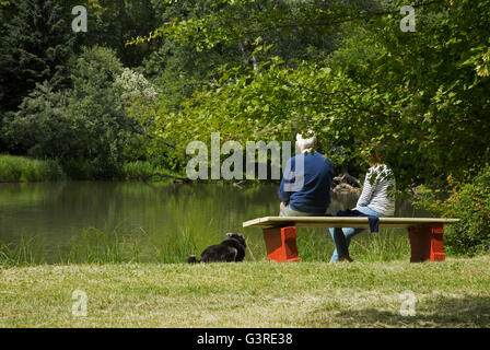 Coppia di anziani con un cane in appoggio su un banco da lo stagno in un parco di Varsavia, una bella giornata di sole nel mese di giugno. Editoriale. Horizont Foto Stock