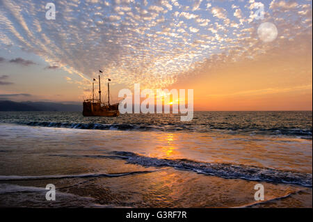 La nave dei pirati fantasy è un vecchio di legno la nave dei pirati con bandiere completo come il sole tramonta sull'oceano e la luna sorge in un colorato s Foto Stock