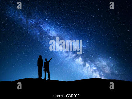 La Via Lattea con la silhouette di una famiglia. Padre e figlio che puntare il dito nella notte cielo stellato sulla montagna. Paesaggio notturno Foto Stock