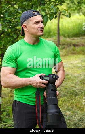 Natura professionale fotografo in possesso di una fotocamera con un grande teleobiettivo Foto Stock