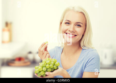 Donna felice di mangiare uva in cucina Foto Stock