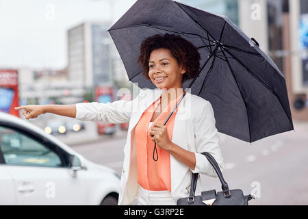 Felice donna africana con ombrello cattura di taxi Foto Stock