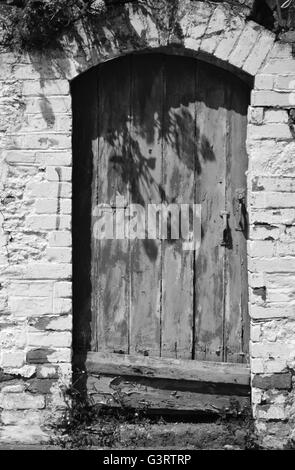 Vecchia porta di legno, vernice scrostata, circondato da muro bianco con portale ad arco alto Foto Stock