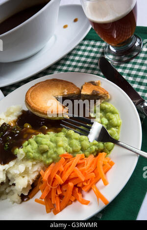 Un classico inglese tradizionale piatto di bistecche, torta di purè di patate, fiacco piselli e carote. Serviti con sugo di carne e un bicchiere di birra. Foto Stock