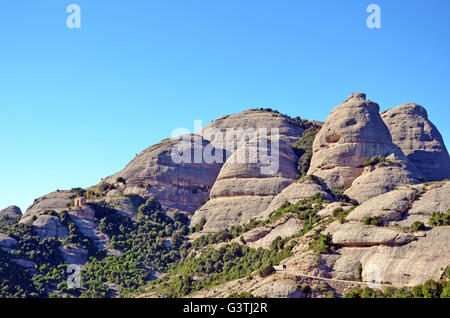 La montagna di Montserrat, Catalogna, Spagna, e la piccola cappella di pietra di Sant Joan sul fianco della montagna Foto Stock
