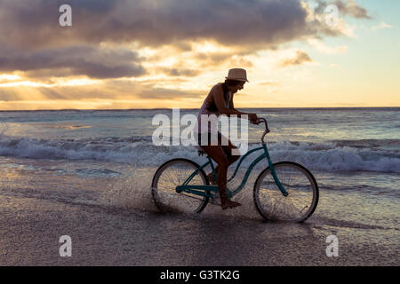 Donna in bicicletta sulla spiaggia Foto Stock