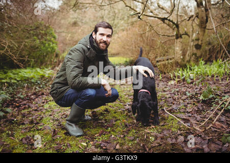 Hipster uomo sorridente alla telecamera mentre accarezzare il suo cane Foto Stock