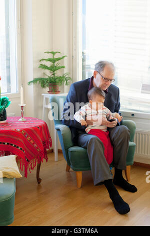 Nonno seduto in poltrona tenendo un neonato Foto stock - Alamy