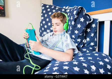 A dieci anni di vecchio ragazzo posa su un letto ascoltando musica in cuffia. Foto Stock