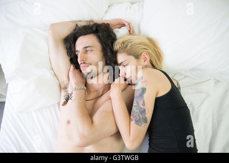 Un giovane tatuato giovane cuddling su un letto. Foto Stock